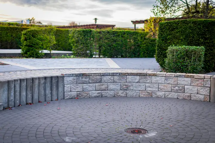 A curved stone retaining wall holding back a planted terrace above a paved circle