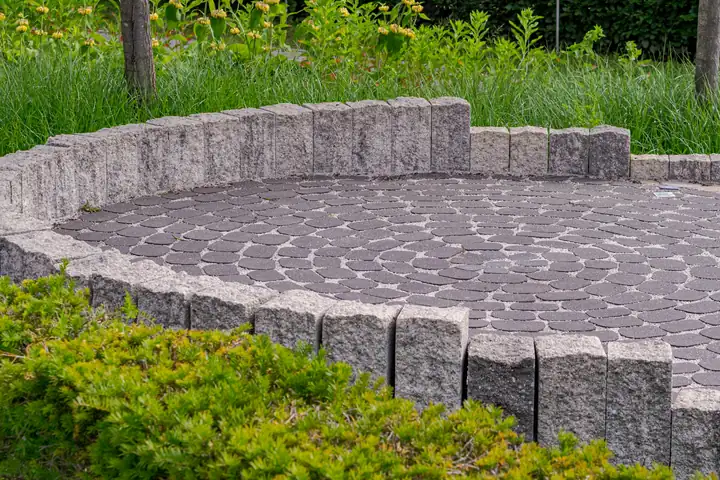 A curved paver terrace with a low seat wall, planted behind with ornamental grasses