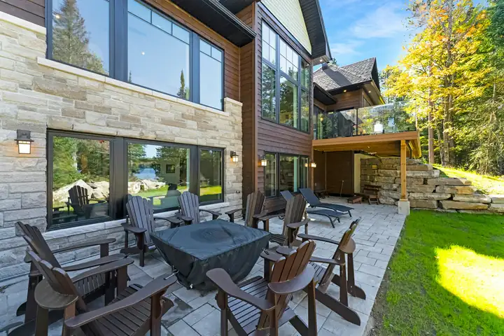A stone terrace with a fire pit and chairs set against the back of a house