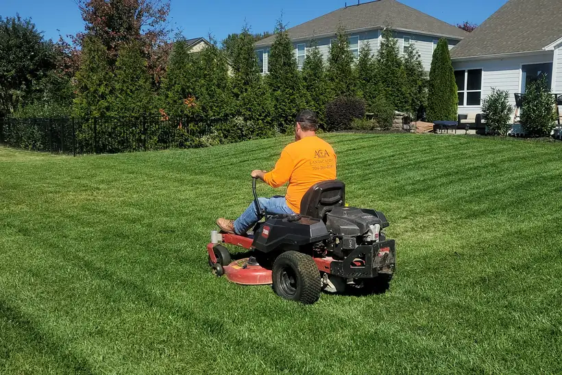 A crew member mowing a striped suburban lawn on a riding mower