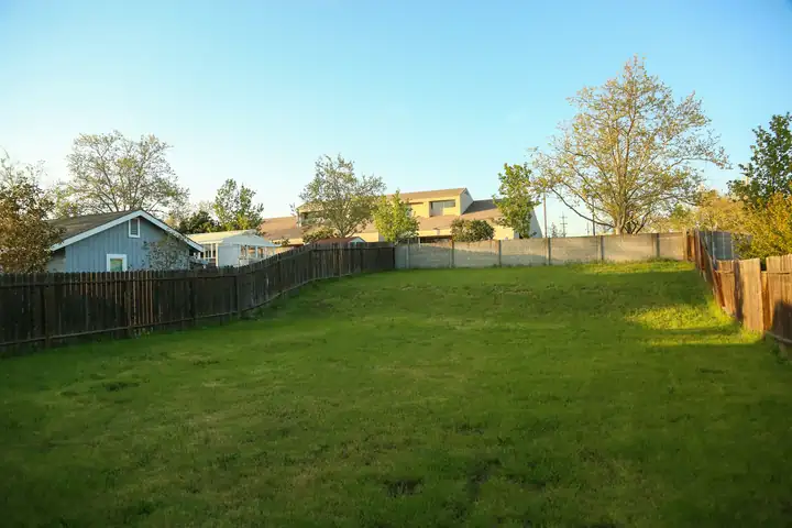 The same back corner before the work: a flat lawn against a board fence, worn bare where water stood